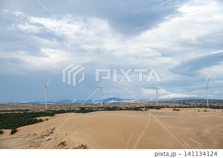 Wind turbines standing on vast sand dunes under an overcast cloudy sky Wind turbines standing on vast sand dunes under an overcast cloudy sky 141134124