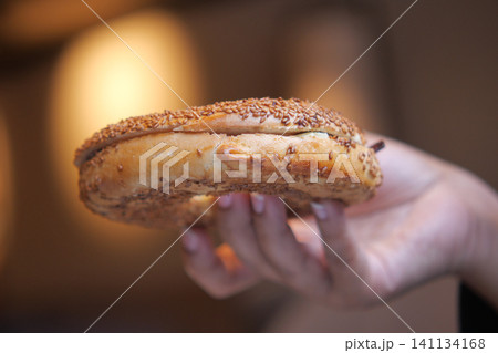 Hand holding a sesame bagel with filling in a cozy setting Hand holding a sesame bagel with filling in a cozy setting 141134168