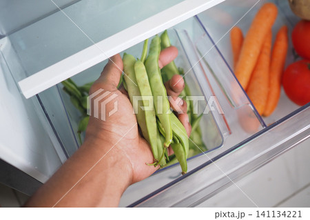 Person holding green beans in a refrigerator 141134221
