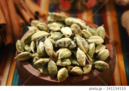 Cardamom pods in a wooden bowl on a colorful table Cardamom pods in a wooden bowl on a colorful table 141134310