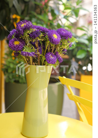 Bright purple flowers in a green vase on a sunny table Bright purple flowers in a green vase on a sunny table 141134363