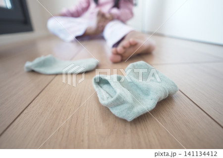 Child playing with socks on wooden floor in a sunny room Child playing with socks on wooden floor in a sunny room 141134412