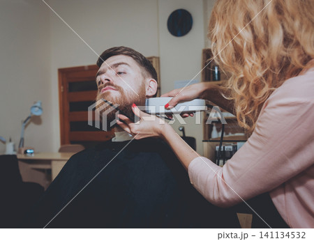 Master cuts hair and beard of men, hairdresser makes hairstyle for a young man. Hipsters Master cuts hair and beard of men, hairdresser makes hairstyle for a young man. Hipsters 141134532