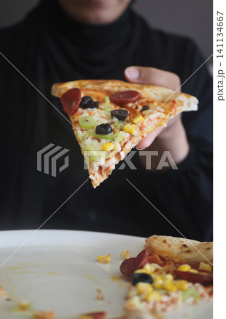 Person holding a slice of pizza with various toppings Person holding a slice of pizza with various toppings 141134667