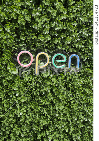 Colorful open sign against green foliage backdrop 141134723