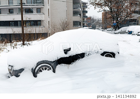 Snow covers a car parked on a street in a city during winter, showing deep snow accumulation 141134892