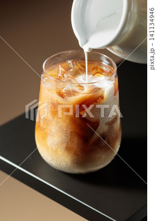Cream is poured into a glass of iced coffee. Cream is poured into a glass of iced coffee. 141134946