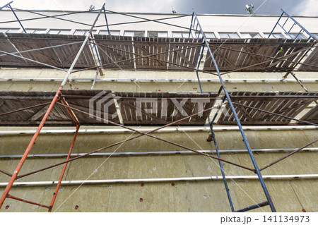 A group of workers builds scaffolding around a building for renovation. The structure is tall and the sky looks cloudy. Work is in progress A group of workers builds scaffolding around a building for renovation. The structure is tall and the sky looks cloudy. Work is in progress 141134973