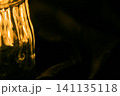 シワのある黒い布の上のガラスコップ越しに見えるロウソクの温かい光 141135118
