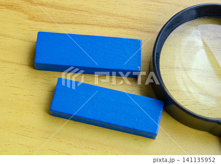 Two blue rectangular wooden blocks beside a magnifying glass on a wooden tabletop with simple layout Two blue rectangular wooden blocks beside a magnifying glass on a wooden tabletop with simple layout 141135952
