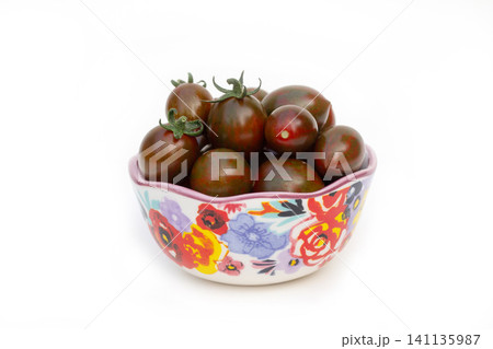 Ceramic floral bowl with dark cherry tomatoes on white. Ceramic floral bowl with dark cherry tomatoes on white. 141135987