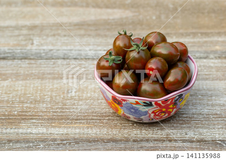 Bowl with black cherry tomatoes on the brown wooden table. Bowl with black cherry tomatoes on the brown wooden table. 141135988