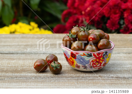 Bowl with black cherry tomatoes in the summer blooming garden. Bowl with black cherry tomatoes in the summer blooming garden. 141135989