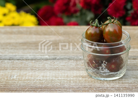 Jar with black cherry tomatoes in the summer blooming garden. Jar with black cherry tomatoes in the summer blooming garden. 141135990