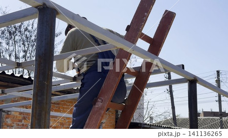 Adult worker polishing iron using electric grinder wheel on carport frame. Professional repairman grinding metal detail with circular saw at construction at sunny day. Male laborer working at the site Adult worker polishing iron using electric grinder wheel on carport frame. Professional repairman grinding metal detail with circular saw at construction at sunny day. Male laborer working at the site 141136265