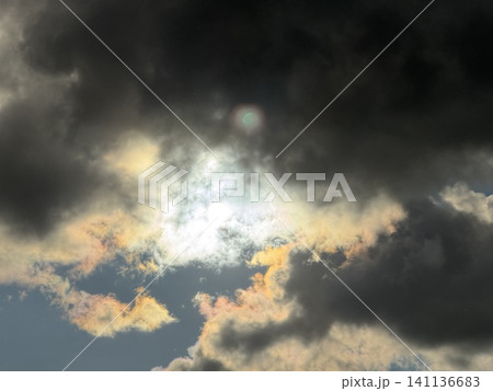 Bright Sunburst Through Dark Ominous Clouds with Iridescent Colors Bright Sunburst Through Dark Ominous Clouds with Iridescent Colors 141136683