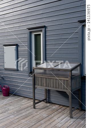 Raised wooden cold frame greenhouse on deck beside modern wooden house Raised wooden cold frame greenhouse on deck beside modern wooden house 141136975