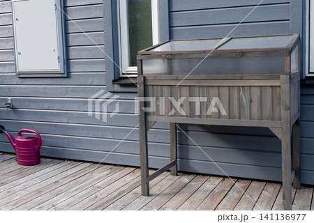 Raised wooden cold frame greenhouse on deck beside modern wooden house Raised wooden cold frame greenhouse on deck beside modern wooden house 141136977