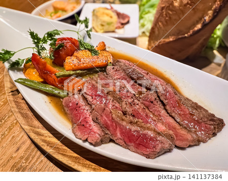 色鮮やかな焼き野菜を添えたジューシーな牛ステーキのカット 色鮮やかな焼き野菜を添えたジューシーな牛ステーキのカット 141137384