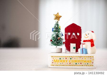 メリークリスマスの文字と並ぶ可愛い雪だるまと赤い家、ツリーの置物 141138492