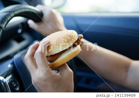 Asian woman driver hold and eat hamburger food in car. 141139409