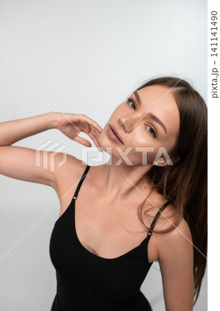 Young woman with natural beauty, glowing skin, and freckles posing elegantly in a black camisole 141141490