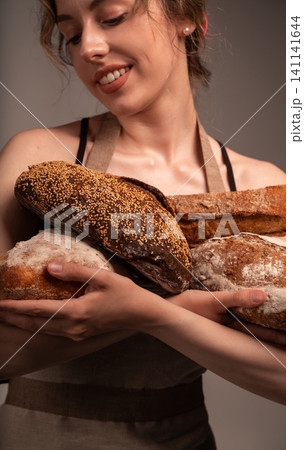 Woman baker holding fresh rustic loaves, offering traditional artisan bread with a smiling face and apron 141141644