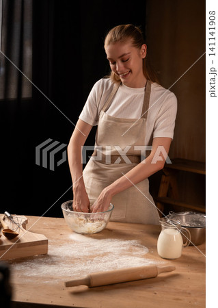 Happy woman kneading dough in the kitchen, enjoying baking fresh bread or pastry from scratch 141141908