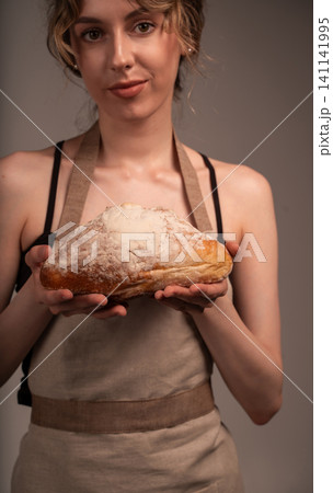 Woman baker wearing apron presenting fresh artisan sourdough bread loaf with flour dusted crust Woman baker wearing apron presenting fresh artisan sourdough bread loaf with flour dusted crust 141141995
