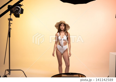 Fashion model posing in bikini and straw hat during studio swimwear photoshoot for summer collection Fashion model posing in bikini and straw hat during studio swimwear photoshoot for summer collection 141142589