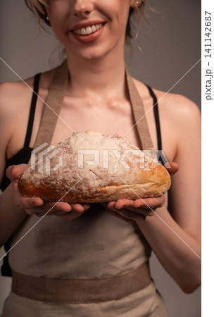 Woman baker holding a freshly baked, crusty sourdough bread loaf with flour dusting, smiling in an artisan apron Woman baker holding a freshly baked, crusty sourdough bread loaf with flour dusting, smiling in an artisan apron 141142687