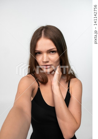 Young woman taking a selfie, expressing confidence and modern individual style with a serious gaze 141142756