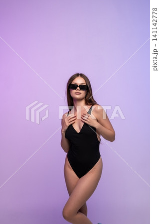 Woman posing in black swimsuit and sunglasses in studio with purple gradient background, embodying summer style and confidence Woman posing in black swimsuit and sunglasses in studio with purple gradient background, embodying summer style and confidence 141142778