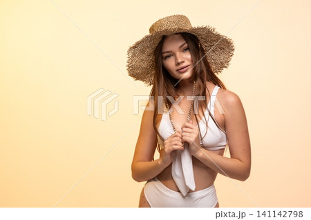 Young woman posing in a studio, wearing a straw hat and white swimsuit, perfect for summer, vacation, and fashion concepts Young woman posing in a studio, wearing a straw hat and white swimsuit, perfect for summer, vacation, and fashion concepts 141142798