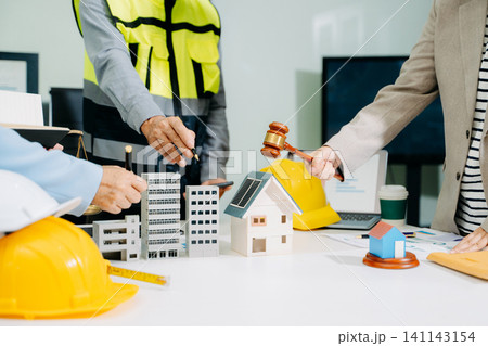 Legal and engineering professionals reviewing building plans with justice scale, gavel and safety equipment, symbolizing construction law, property regulation 141143154
