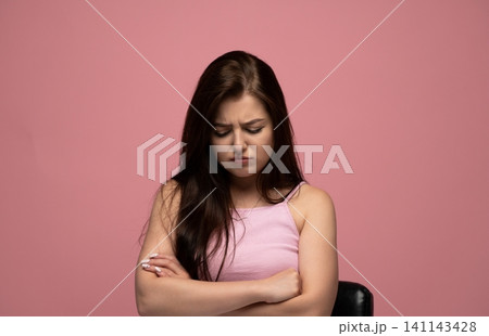 Young woman looking down with a disappointed facial expression, arms crossed, expressing frustration and unhappiness Young woman looking down with a disappointed facial expression, arms crossed, expressing frustration and unhappiness 141143428