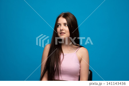 Young woman with long brown hair wearing a pink crop top, looking sideways with a thoughtful expression Young woman with long brown hair wearing a pink crop top, looking sideways with a thoughtful expression 141143436