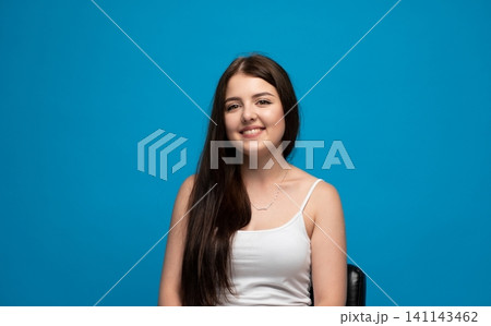 Young woman smiling, expressing happiness and positive emotion on blue background, looking at camera in studio 141143462