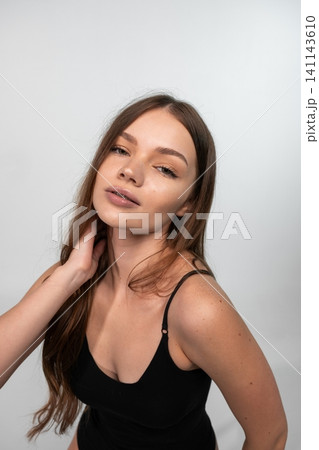 Young woman with natural long hair posing confidently, touching neck, looking at camera in studio Young woman with natural long hair posing confidently, touching neck, looking at camera in studio 141143610