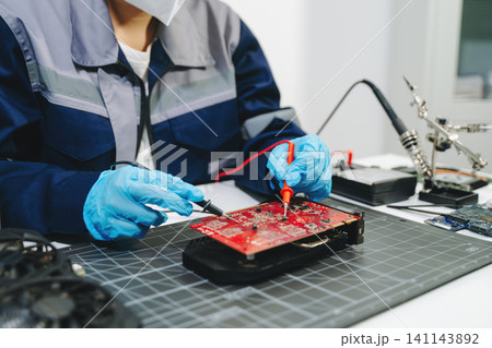 Professional technician repairing a graphics card PCB using soldering equipment. Ideal for technology, electronics repair, engineering and IT service concepts. Professional technician repairing a graphics card PCB using soldering equipment. Ideal for technology, electronics repair, engineering and IT service concepts. 141143892