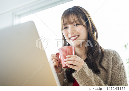 コーヒーを飲みながらパソコンで仕事をする若い女性 141145153