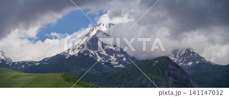 Panoramic Caucasus mountains landscape with Mount Kazbek peak and green hills Panoramic Caucasus mountains landscape with Mount Kazbek peak and green hills 141147032
