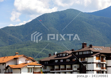 Bansko, Bulgaria, red emergency medical service helicopter flying over the town buildings, green Pirin mountains Bansko, Bulgaria, red emergency medical service helicopter flying over the town buildings, green Pirin mountains 141149981