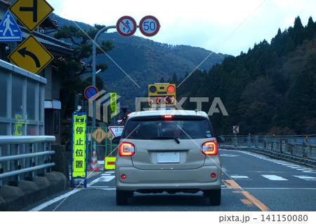 山間部の道路における通行規制(交互通行)、移動式信号で停車中の乗用車(後続車から撮影) 山間部の道路における通行規制(交互通行)、移動式信号で停車中の乗用車(後続車から撮影) 141150080