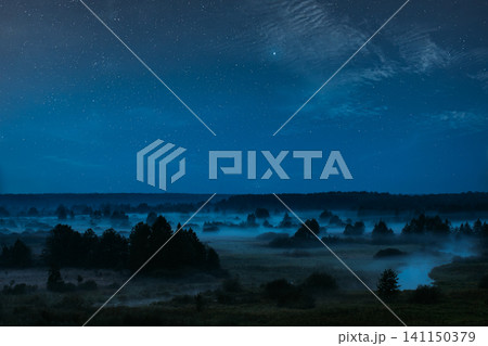 Misty rural landscape with trees and a river under a starry night sky. Misty rural landscape with trees and a river under a starry night sky. 141150379