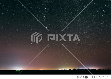 starry night sky over a dark horizon with distant city lights. starry night sky over a dark horizon with distant city lights. 141150382