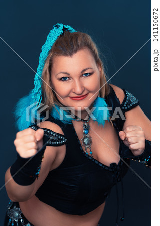 Woman dancer in black costume with blue feathers posing in fighting stance. Tribal fusion dancer character portrait for stage Woman dancer in black costume with blue feathers posing in fighting stance. Tribal fusion dancer character portrait for stage 141150672
