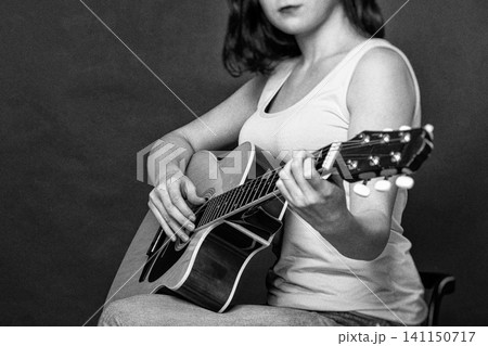 Young woman playing Spanish six string acoustic guitar in retro style. Monochrome photography with film grain and selective focus. Hobby, creativity and music education concept 141150717