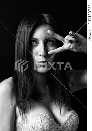Woman portrait in black and white with retro style. Lady showing peace sign gesture on dark background. Artistic analog photography with film grain 141150720