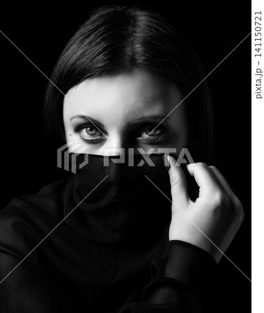 Portrait of woman covering face with black veil. Monochrome artistic photography with grainy texture. Mysterious emotional concept, retro analog film style, dramatic lighting and intense gaze Portrait of woman covering face with black veil. Monochrome artistic photography with grainy texture. Mysterious emotional concept, retro analog film style, dramatic lighting and intense gaze 141150721